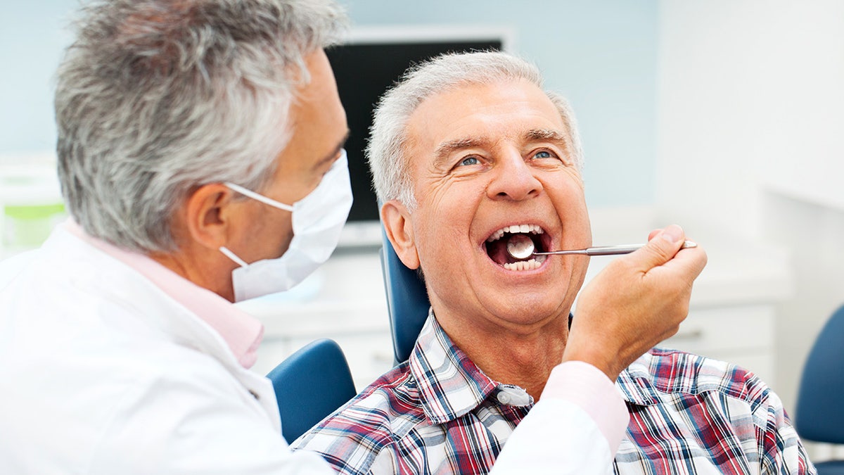 The dentist's senior man who examines his teeth while a dental mirror is put in his mouth and look forward sitting on his chair